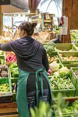 Frau räumt im Supermarkt Gemüse ein