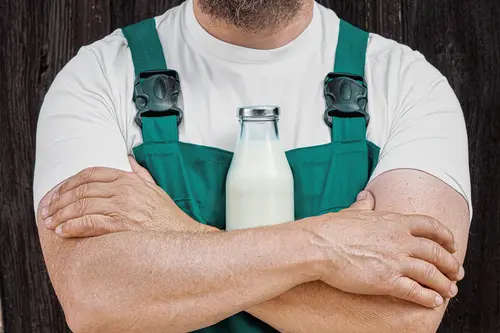 Landwirt verschränkt Arme vor einer Milchflasche vor der Brust 
